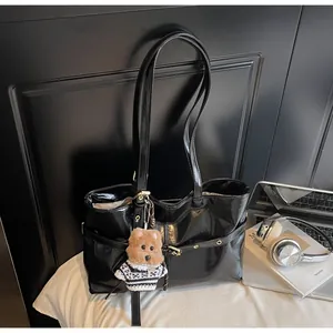 Détail d'un sac cabas en cuir ciré noir brillant avec un charm ours et poches à rivets
