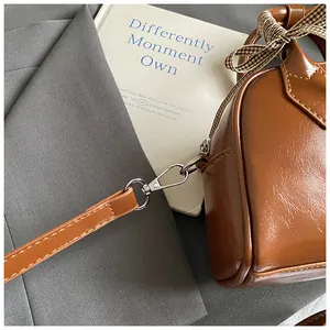 Detail of a brown leather satchel with silver hardware and a plaid ribbon on a grey suit