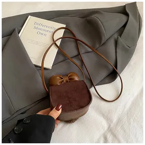 Dettaglio mini borsa a sella con fiocco in pelle e texture scamosciata marrone su bianco