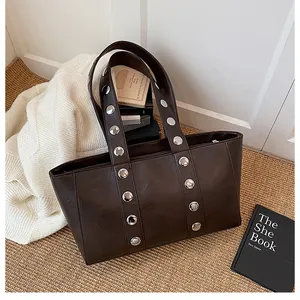 Detailed shot of dark brown tote bag with large silver studs on shoulder straps