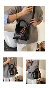 Detail of black faux crocodile leather bucket bag with a red bear charm and strap
