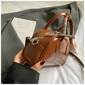 Detail of brown faux leather handbag featuring a silk scarf bow and fluffy charm