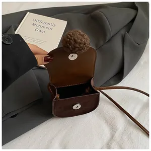 Dettaglio della borsa a tracolla marrone per bambina con pompon e chiusura magnetica