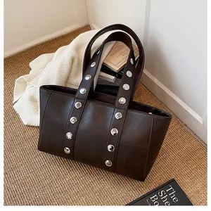 Detail of silver rivets on a brown faux leather tote bag over a straw mat background