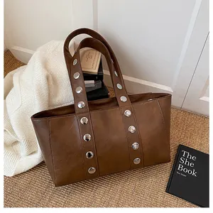 Detail view of brown leather shoulder bag with silver metal studs and wide strap