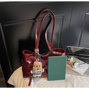 Détail d'un sac cabas en cuir brillant rouge foncé avec bandoulières et breloque ours