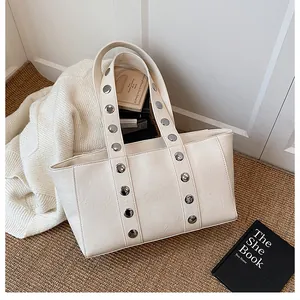 Close-up of beige faux leather tote bag with silver metal rivets on a cozy home setting
