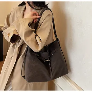 Detail of dark brown tote bag with matte texture and gold ring hardware on beige coat
