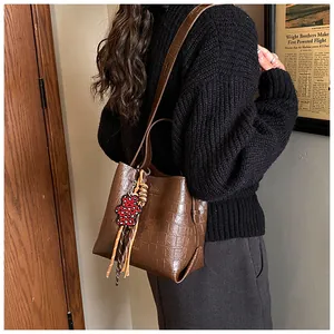 Brown crocodile pattern bucket bag with a cute red bear charm on a female model