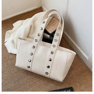 Detail of off-white tote bag with silver studs and books inside showing large capacity