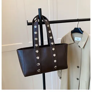 Detail of dark brown tote bag featuring silver metal rivets on textured faux leather