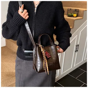 Detail of dark brown faux leather bucket bag with crocodile texture and bear charm