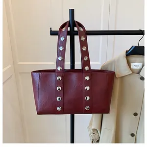 Detailed close-up of dark red leather tote bag with stylish silver metal rivets