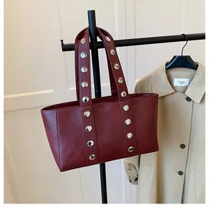 Close-up of deep red tote bag featuring vintage silver metal rivets and textured PU leather