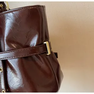 Gros plan sur le cuir ciré brillant et la boucle en métal doré du sac fourre-tout bordeaux