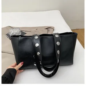 Detail of black matte leather tote bag featuring silver metal rivets on shoulder strap