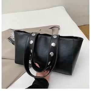 Detail of black PU leather tote bag featuring large silver metal rivets on the shoulder strap