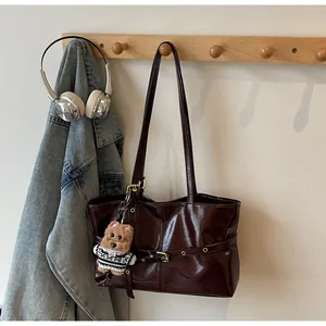 Détail du sac cabas en cuir verni bordeaux avec boucles métalliques et charm d'ours brun