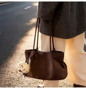 Close-up of brown suede tote bag with slim straps and a plush charm in sunset light