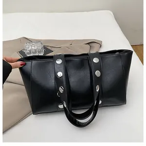 Detail of black faux leather tote with silver stud accents and zipper on a neutral background