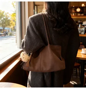 Detail of dark brown suede tote bag with plush pendant on a textured grey coat