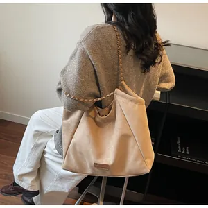 Détail du cabas en daim beige montrant la bandoulière en chaîne et l'écusson logo en cuir