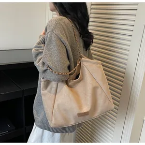 Détail du grand sac cabas beige en daim avec bandoulière chaîne porté par un mannequin