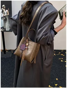 Brown crocodile-textured bucket bag with leopard floral charm on a grey wool coat
