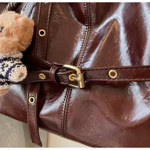 Détail du cabas en cuir ciré marron foncé avec œillets dorés et breloque ours en peluche