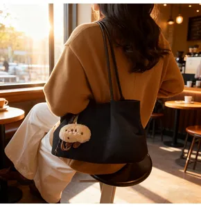 Close-up of black suede tote bag with plush charm styled on a model in a cozy cafe setting