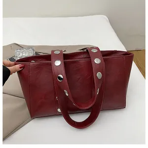 Detail of burgundy leather tote bag with wide straps and silver round metal rivets