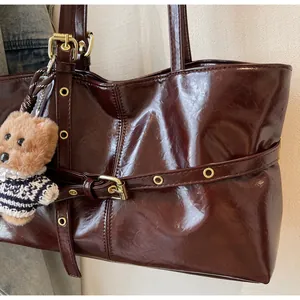 Détail d'un cabas en cuir ciré marron foncé avec boucles dorées et breloque ours