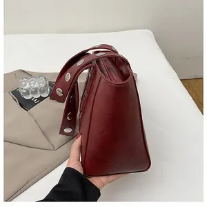 Detail view of burgundy PU leather shoulder bag with silver rivet studs on the strap