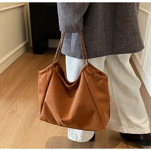 Détail d'un grand sac cabas en daim marron avec des bandoulières à chaînes élégantes