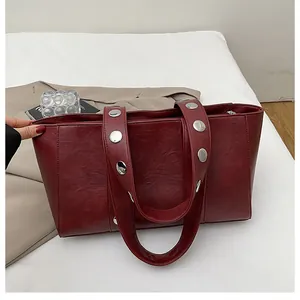 Detail of dark red tote bag featuring wide strap with large silver metal rivets