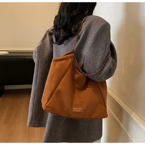 Détail du sac cabas en daim marron avec bandoulière chaîne et écusson en cuir