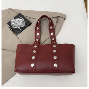 Macro view of dark red tote bag featuring large silver metal rivets on leather strap