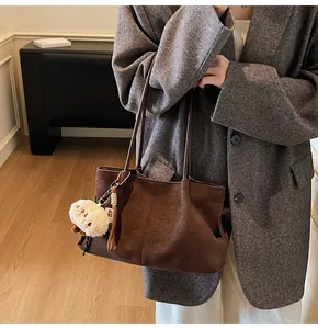Detail of vintage brown suede tote bag featuring a cute white plush doll charm
