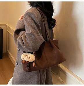 Detail of dark brown suede tote bag with cute plush pendant on grey tweed coat