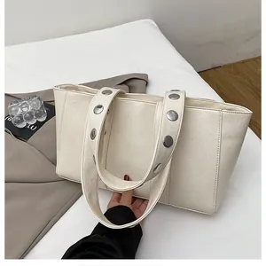 Detail of cream white tote bag featuring large silver metal rivets and leather texture