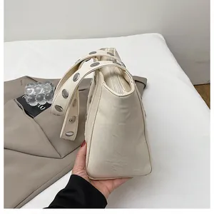 Close-up of silver metal studs on a cream white leather tote bag with a zipper top