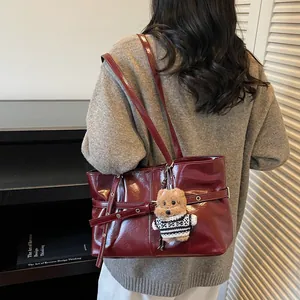 Sac fourre-tout minimaliste en cuir bordeaux avec pendentif ours sur l'épaule d'un mannequin