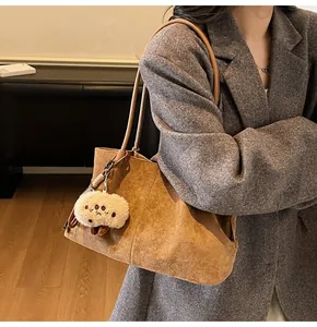 Close-up of brown suede tote bag on a model wearing a grey wool coat with plush charm