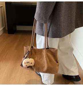 Detail of brown suede tote bag featuring a cute beige plush sheep charm and dual straps