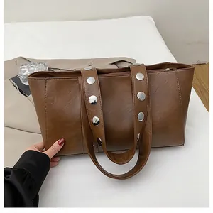 Detail view of brown leather tote bag featuring stylish silver rivets on wide shoulder straps