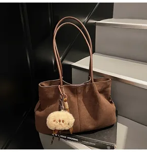 Close-up of brown suede underarm tote bag with a soft plush doll pendant on the side
