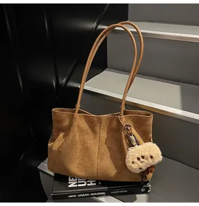 Detailed close-up of brown suede tote bag with stylish plush pendant on a book