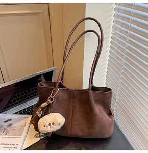 Detailed view of brown suede tote bag with plush charm in a minimalist office setting