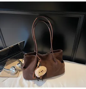 Detail of dark brown suede tote bag with pleated side and cute plush charm on white table