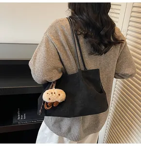 Detail of a black suede tote bag with plush bear charm and slender shoulder straps